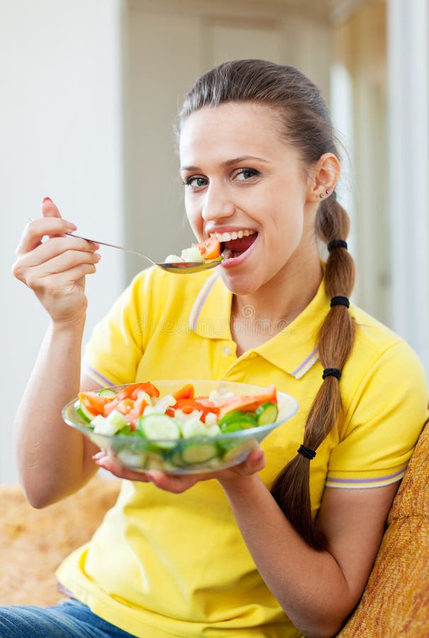 Femme mangeant de la salade de légumes sur le sofa photo stock Femme mangeant de la salade de légumes sur le sofa photo stock