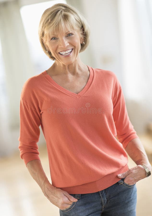 Femme mûre avec des mains dans des poches se tenant à la maison images stock Femme mûre avec des mains dans des poches se tenant à la maison images stock