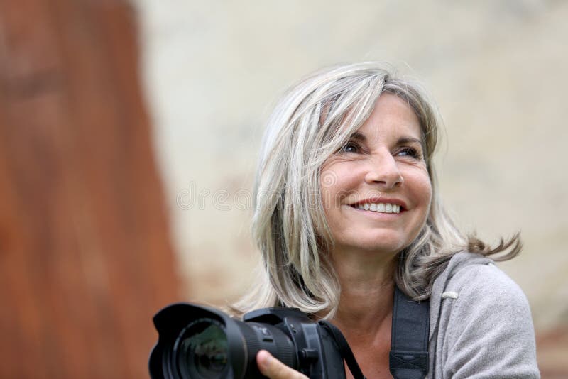 Femme mûre de sourire tenant un appareil-photo photographie stock libre de droits Femme mûre de sourire tenant un appareil-photo photographie stock libre de droits