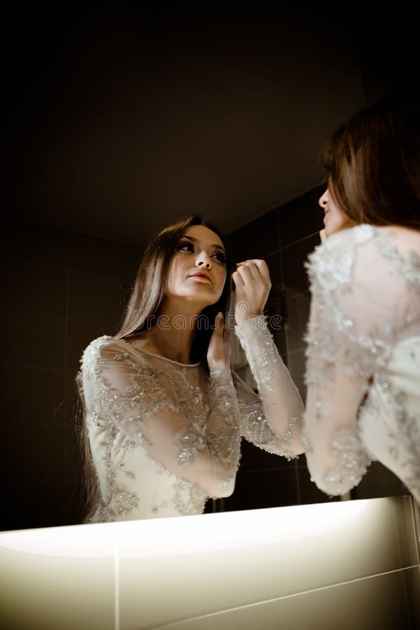 Femme magnifique de brune avec de longs cheveux et yeux bleus se regardant dans le miroir et faisant le maquillage photos libres de droits Femme magnifique de brune avec de longs cheveux et yeux bleus se regardant dans le miroir et faisant le maquillage photos libres de droits