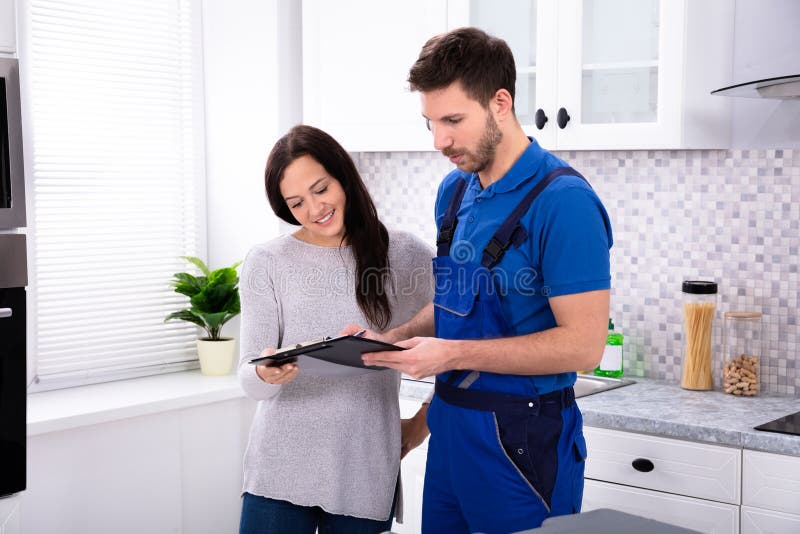 Close-up Of Young Male Plumber Showing Invoice To Woman In Kitchen. Close-up Of Young Male Plumber Showing Invoice To Woman In Kitchen