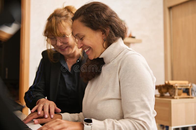 Femme mature mettant sa main sur la main de l'étudiant montrant sa position des doigts sur les touches de piano pendant la leçon d photos libres de droits