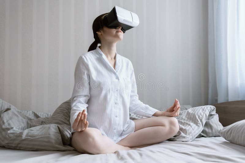 Femme moderne s'asseyant dans le lit dans des pyjamas et méditant en verres de réalité virtuelle photos libres de droits Femme moderne s'asseyant dans le lit dans des pyjamas et méditant en verres de réalité virtuelle photos libres de droits