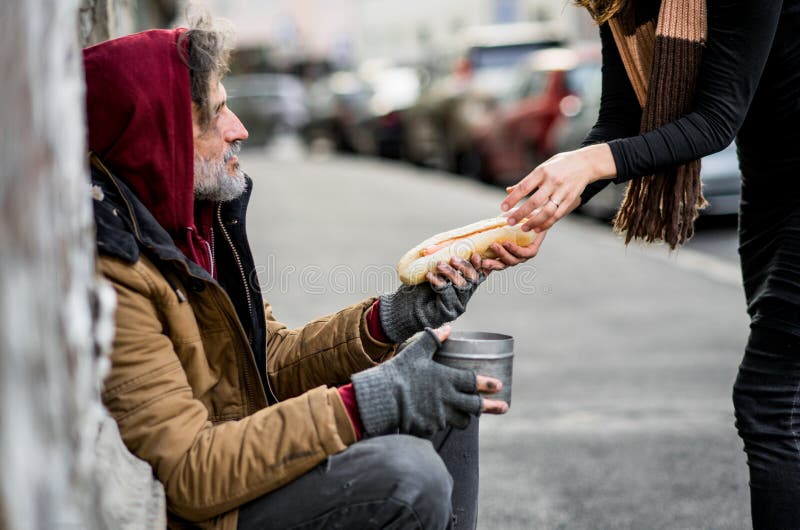 Femme méconnaissable donnant la nourriture à l'homme sans abri de mendiant s'asseyant dans la ville