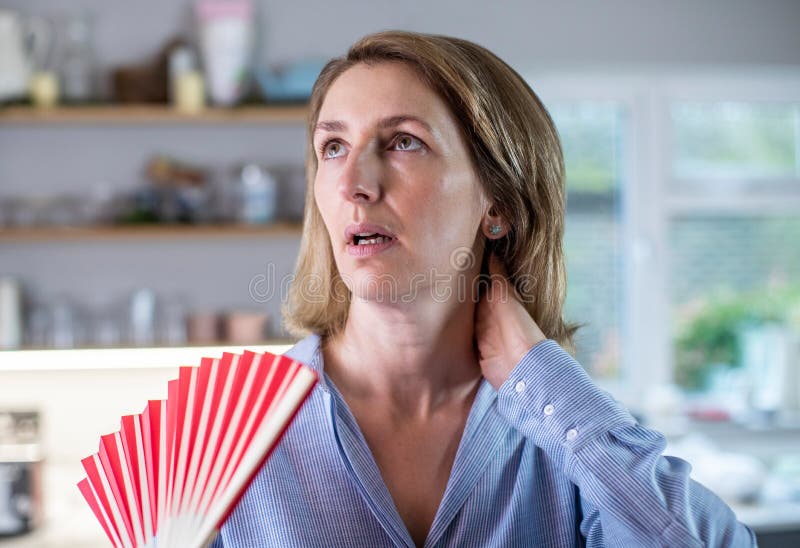 Femme mûre souffrant de bouffées de chaleur de la ménopause en utilisant le ventilateur