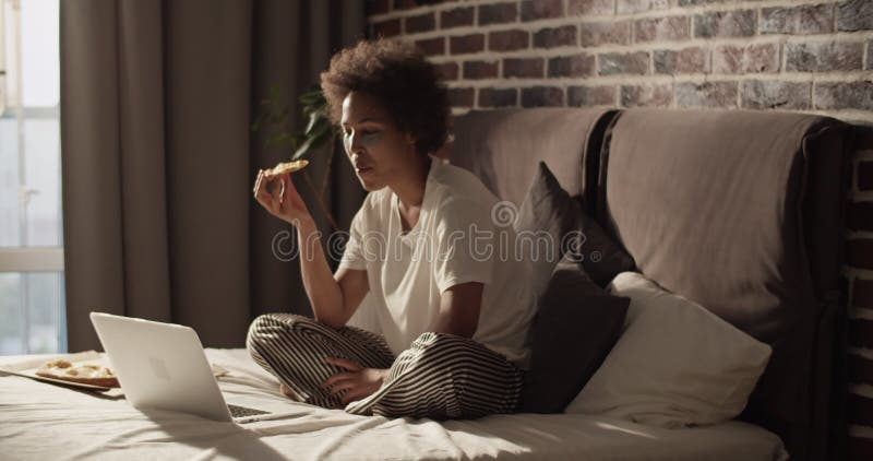 Femme noire heureuse mangeant de la pizza et naviguant netbook banque de vidéos