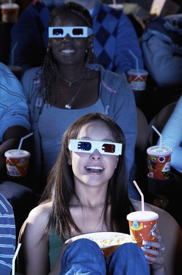 Young women with drink and popcorn watching 3D movie in theater. Young women with drink and popcorn watching 3D movie in theater