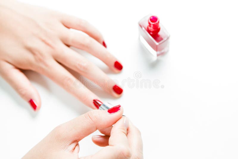 Woman painting her nails with red nail polish against white background. Woman painting her nails with red nail polish against white background