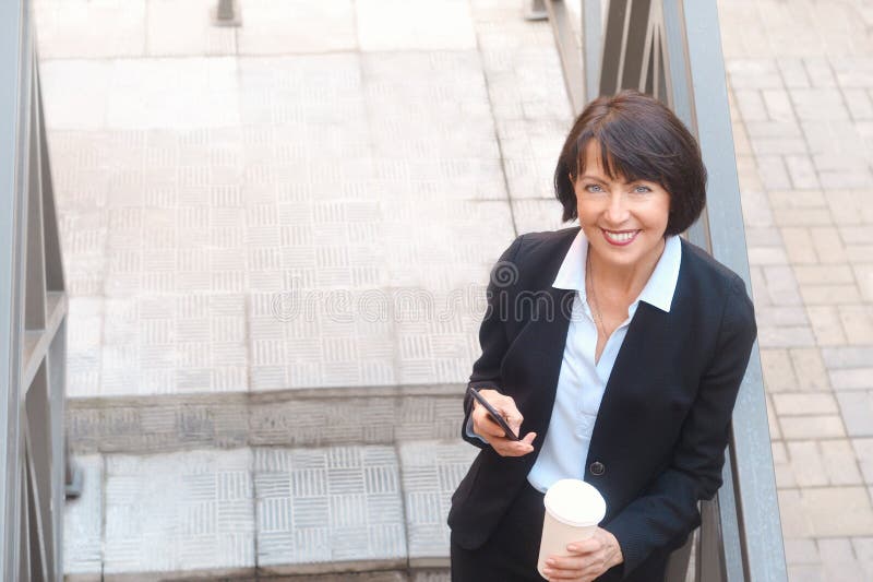 Femme pluse? g? d'affaires avec du caf? , utilisant le t? l? phone portable, ext? rieur photographie stock libre de droits