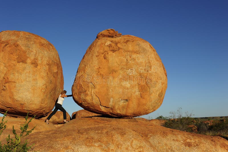 In a sisyphean task a woman in high heel shoes tries to push a huge boulder. In a sisyphean task a woman in high heel shoes tries to push a huge boulder.