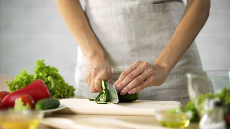 Femme préparant la salade à la cuisine, mains femelles coupant le concombre, suivant un régime photographie stock Femme préparant la salade à la cuisine, mains femelles coupant le concombre, suivant un régime photographie stock
