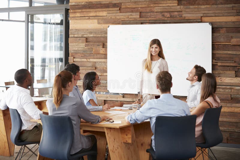 Femme présentant un exposé au tableau blanc à l'équipe d'affaires photographie stock Femme présentant un exposé au tableau blanc à l'équipe d'affaires photographie stock