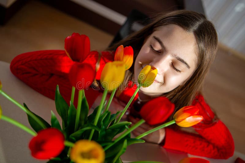 Femme qui aime l'odeur des tulipes vibrantes. Une jeune femme en chandail rouge sourit paisiblement les yeux fermés quand elle photo libre de droits