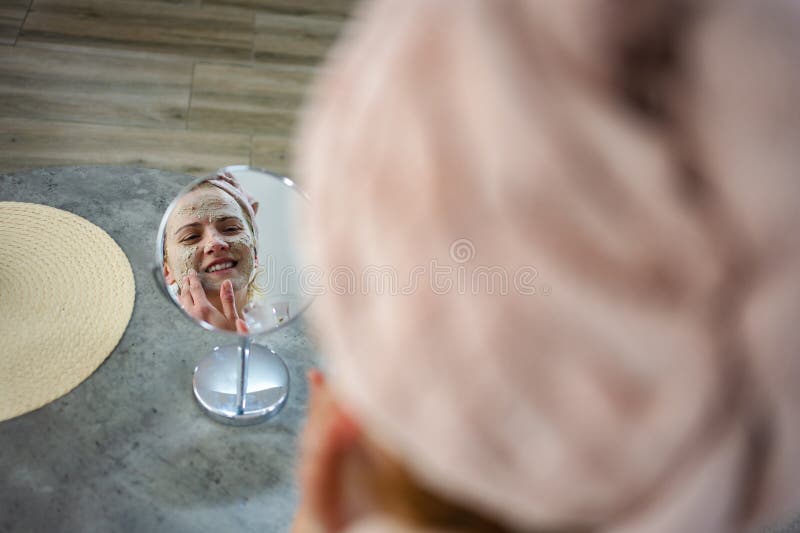 Femme qui applique un masque facial et regarde dans le miroir photo libre de droits