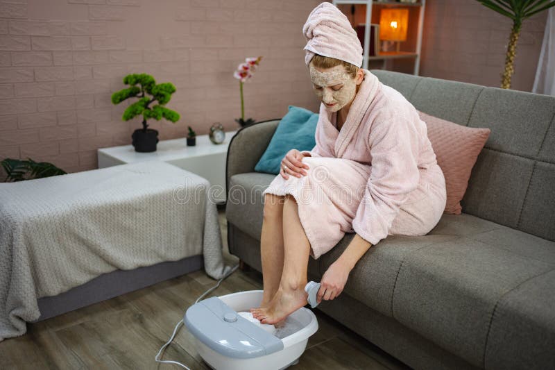 Femme qui profite d'un bain de pieds relaxant à la maison avec masque et peignoir photographie stock