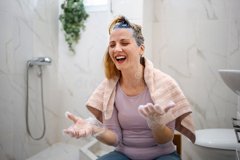 Femme qui rit en teignant ses cheveux bleu dans la salle de bain photo libre de droits