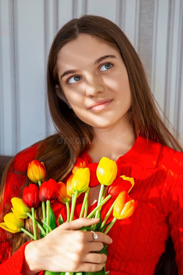 Femme réfléchie tenant bouquet de tulipe vibrant. Une jeune femme en chandail rouge regarde attentivement tout en tenant un images stock