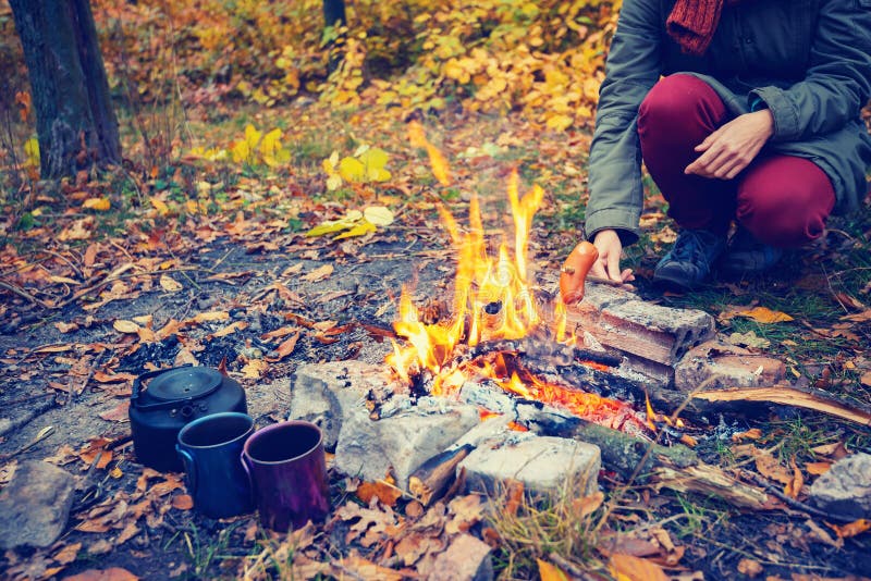 Femme rôtissant une saucisse sur un feu photo stock Femme rôtissant une saucisse sur un feu photo stock