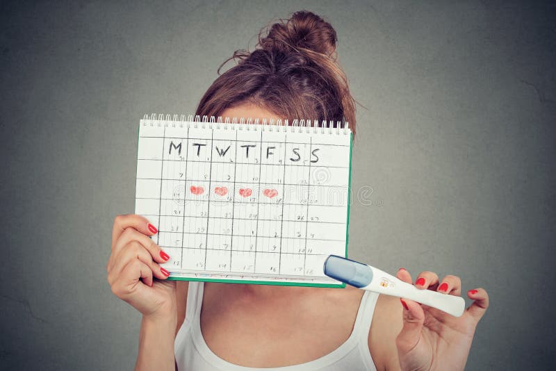 Femme se cachant derrière un calendrier de périodes et montrant un essai de grossesse positif photographie stock libre de droits Femme se cachant derrière un calendrier de périodes et montrant un essai de grossesse positif photographie stock libre de droits