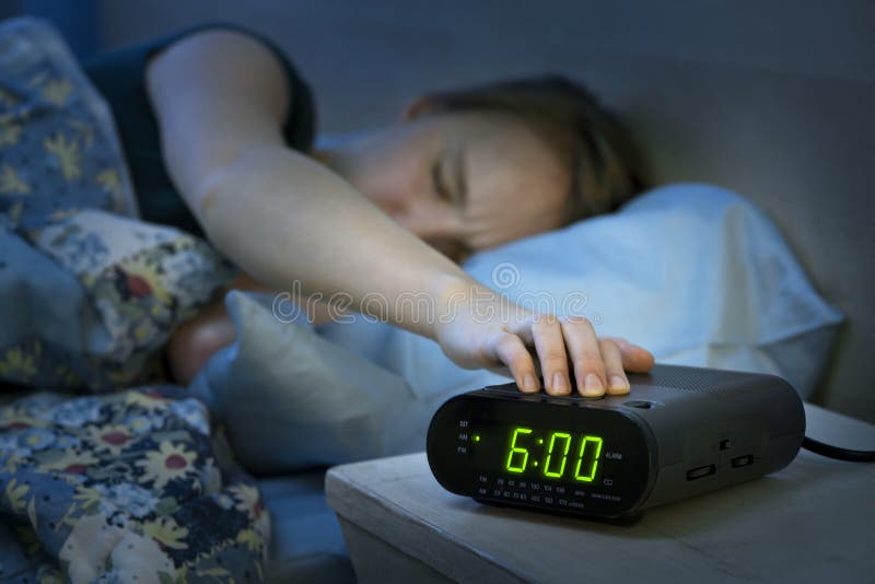 Young woman pressing snooze button on early morning digital alarm clock radio. Young woman pressing snooze button on early morning digital alarm clock radio