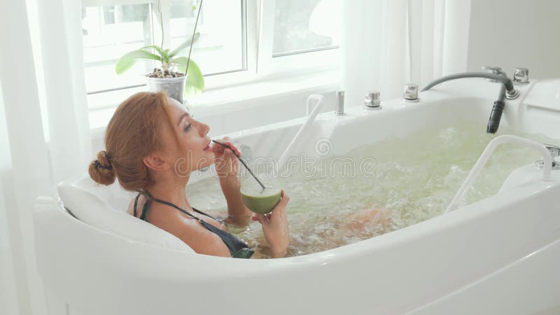Femme sereine bénéficiant d'un smoothie détox dans un bain hydromassant banque de vidéos