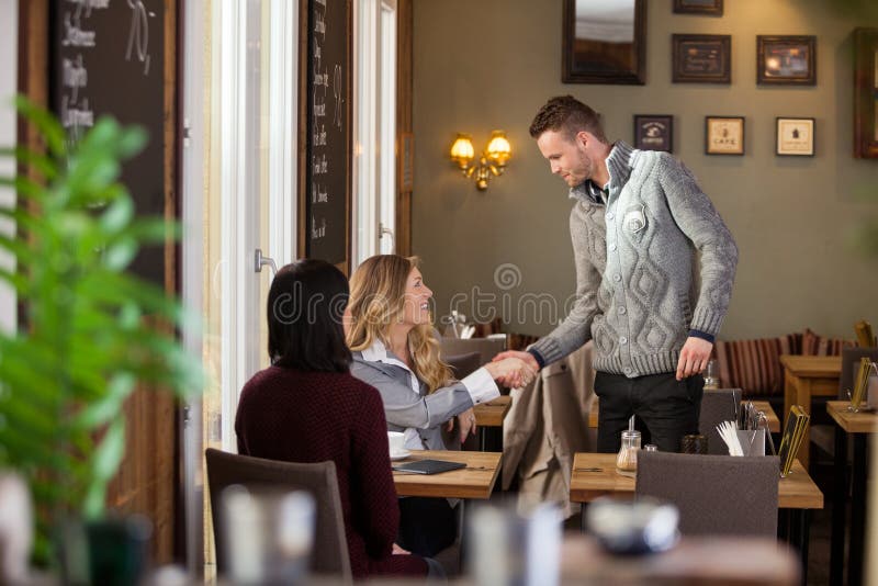 Young women shaking hands with male friend at cafe. Young women shaking hands with male friend at cafe