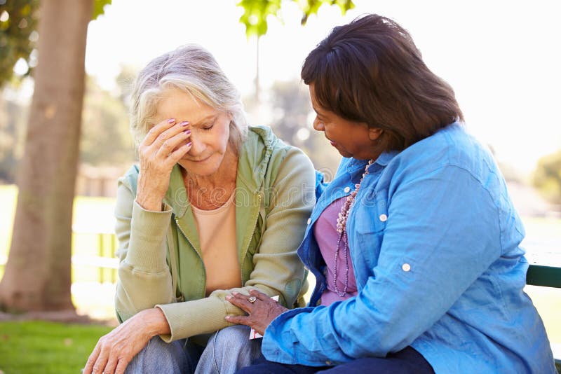 Woman Comforting Unhappy Senior Friend Outdoors Sitting On Bench. Woman Comforting Unhappy Senior Friend Outdoors Sitting On Bench