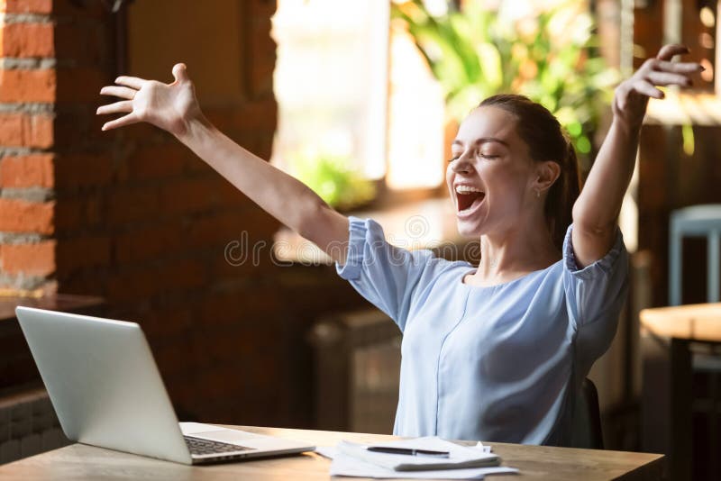 Femme souriante exaltée célébrant la victoire en ligne, en utilisant un ordinateur portable dans un café