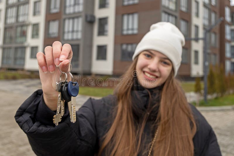 Femme souriante tenant les clés de la maison à l'extérieur. une jeune femme portant une beanie blanche et une veste noire tient un photographie stock libre de droits
