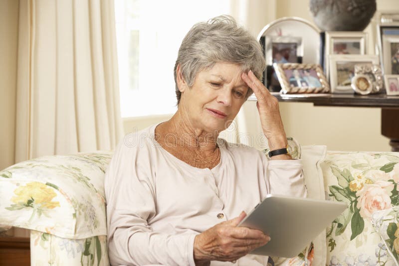 Femme supérieure retirée frustrante s'asseyant sur la Tablette de Sofa At Home Using Digital image libre de droits Femme supérieure retirée frustrante s'asseyant sur la Tablette de Sofa At Home Using Digital image libre de droits