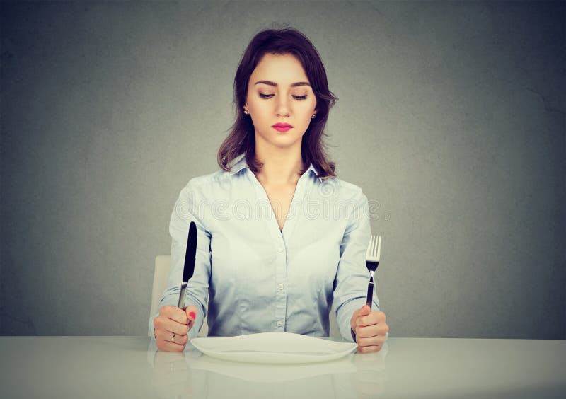 Femme sérieuse avec la fourchette et couteau se reposant à la table avec le plat vide photo libre de droits Femme sérieuse avec la fourchette et couteau se reposant à la table avec le plat vide photo libre de droits