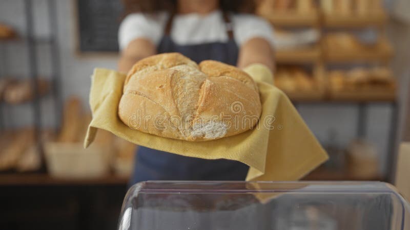 Femme tenant un pain d'or à l'intérieur de la boulangerie avec du pain à l'arrière-plan présentant des produits frais à l'intérieu photo libre de droits