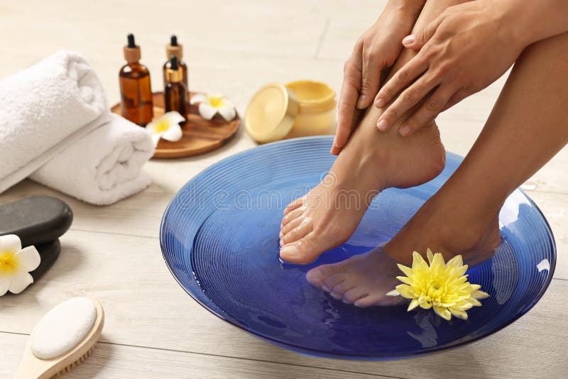 Femme trempant ses pieds dans un bol avec de l'eau et des fleurs sur le closeuse du sol. Soins corporels photographie stock libre de droits