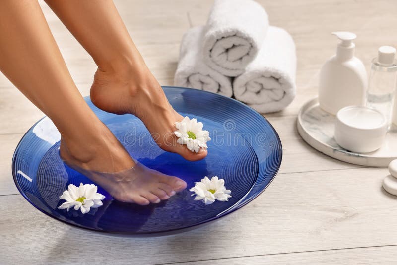 Femme trempant ses pieds dans un bol avec de l'eau et des fleurs sur le closeuse du sol. Soins corporels photo stock