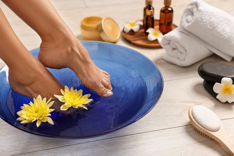 Femme trempant ses pieds dans un bol avec de l'eau et des fleurs sur le closeuse du sol. Soins corporels photos libres de droits