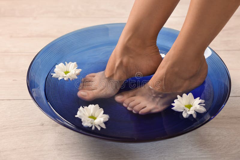Femme trempant ses pieds dans un bol avec de l'eau et des fleurs sur le closeuse du sol. Soins corporels images libres de droits