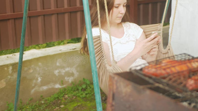 Femme utilise un smartphone. repos extérieur dans la cour de la maison. communiquer avec des amis dans la nature l'internet banque de vidéos