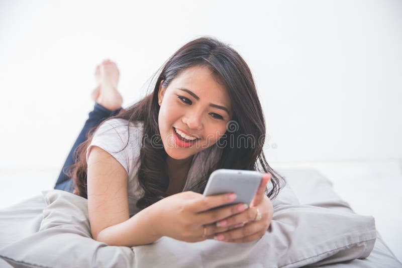 Femme à l'aide du téléphone portable sur le lit image libre de droits Femme à l'aide du téléphone portable sur le lit image libre de droits