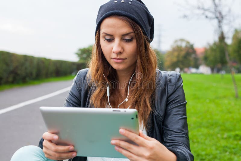 Femme à la mode avec les écouteurs de port de tablette dehors image libre de droits Femme à la mode avec les écouteurs de port de tablette dehors image libre de droits