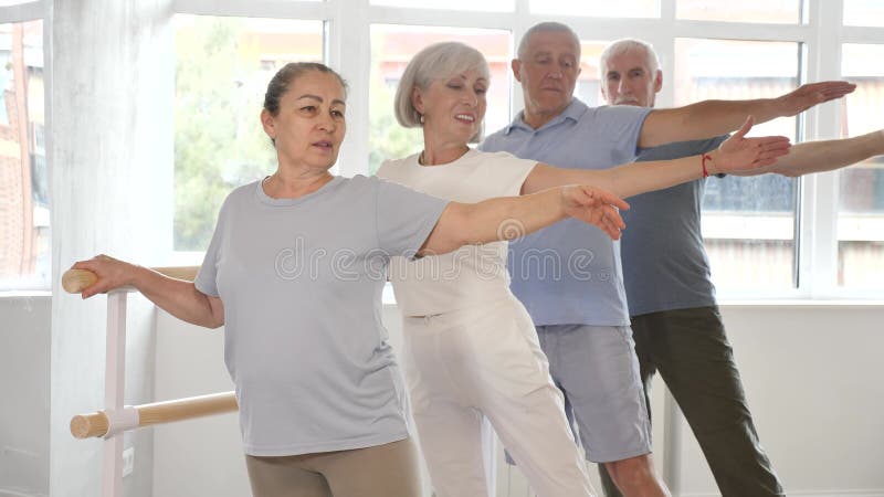 Femme âgée active enseigne diverses poses de ballet pendant les cours de groupe avec des danseurs de ballet à la barre dans banque de vidéos