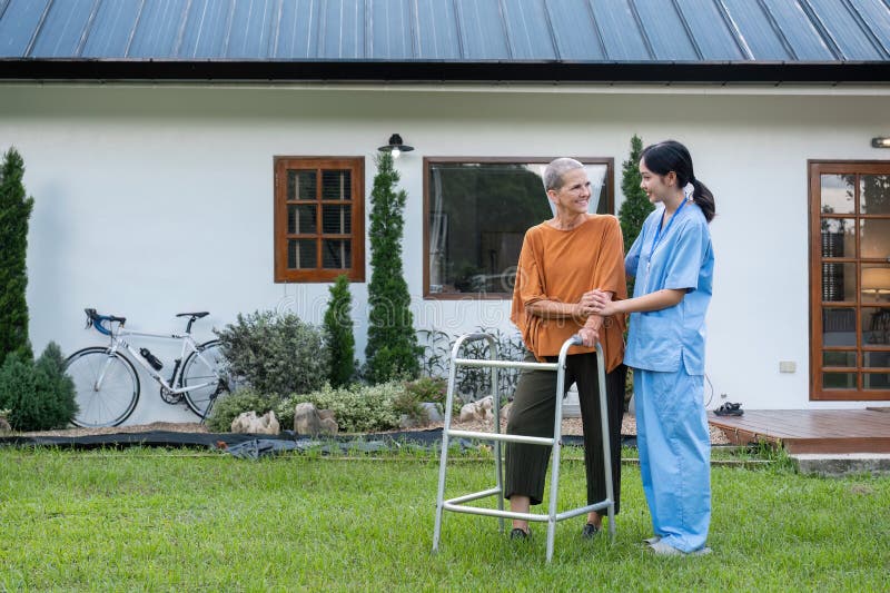 Femme âgée avec soignant marchant dans le jardin à l'extérieur de la maison bénéficiant de l'air frais et de la nature soins et so images libres de droits