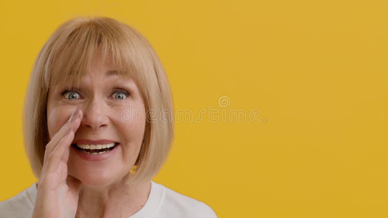Femme âgée excitée partageant des secrets à la caméra en tenant main près de la bouche