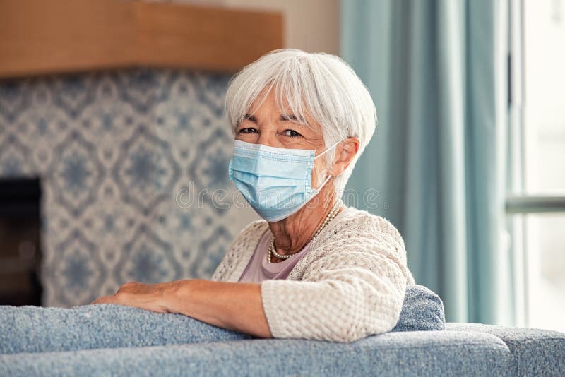 Portrait of smiling old woman wearing face mask at home. Elderly happy grandmother wearing surgical face mask and looking at camera during the lockdown due to coronavirus. Beautiful healthy lady during the covid-19 pandemic stay at home. Portrait of smiling old woman wearing face mask at home. Elderly happy grandmother wearing surgical face mask and looking at camera during the lockdown due to coronavirus. Beautiful healthy lady during the covid-19 pandemic stay at home