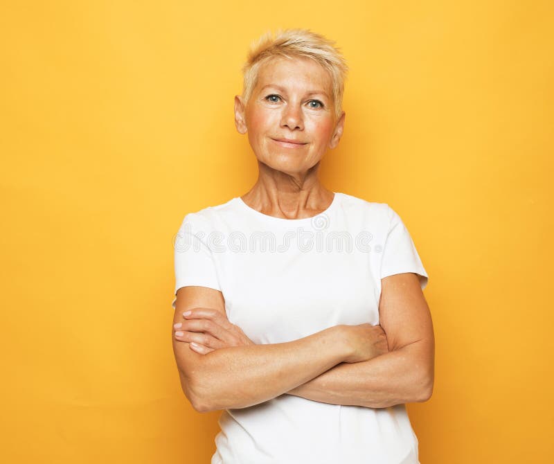 Femme âgée pensionnée souriante aux bras croisés gros portrait sur fond jaune. image libre de droits