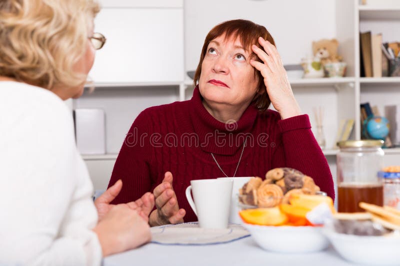 Stressed senior woman having conversation with female over cup of coffee at home. Stressed senior woman having conversation with female over cup of coffee at home