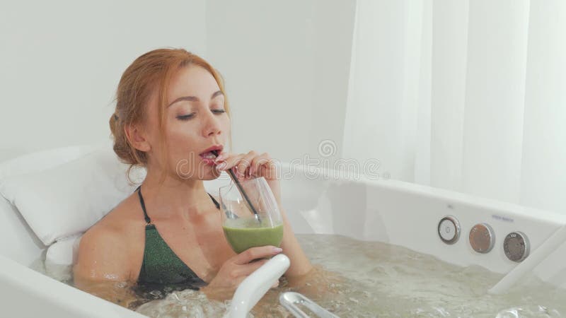 Femme élégante savourant un smoothie rafraîchissant dans un bain à remous luxueux banque de vidéos