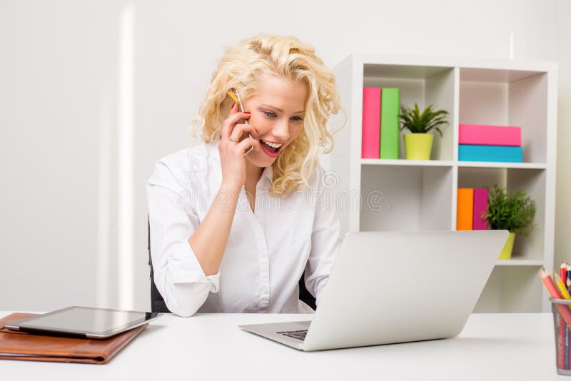 Femme étonnée au bureau utilisant le téléphone et l'ordinateur image stock Femme étonnée au bureau utilisant le téléphone et l'ordinateur image stock