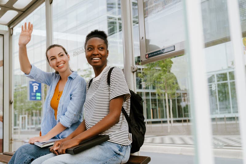 Femmes multiraciales agitant la main et souriant ensemble en étant assise dans le bus photographie stock libre de droits