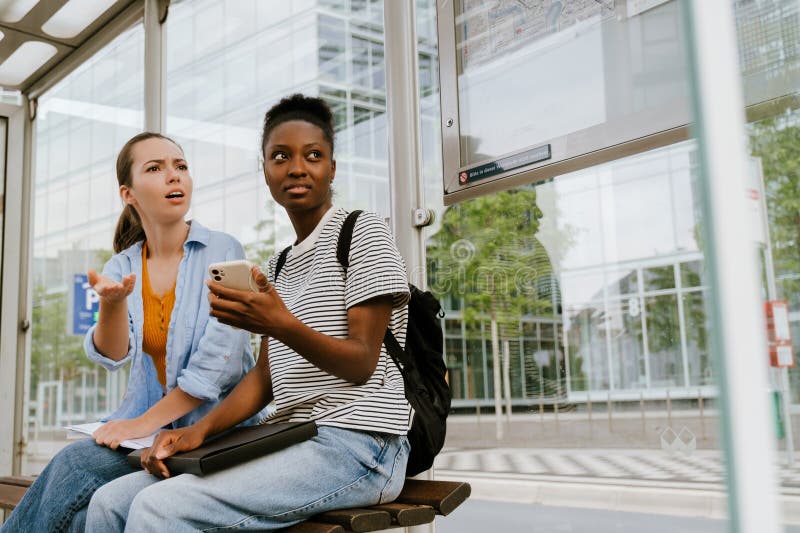 Femmes multiraciales utilisant un téléphone portable ensemble pendant qu'elles sont assis dans le bus image stock