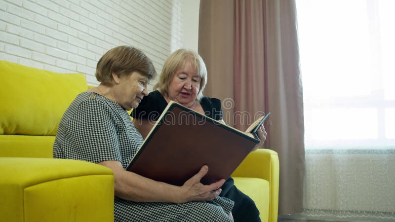 Femmes âgées partageant des souvenirs explorant l'album photo ensemble sur un canapé banque de vidéos